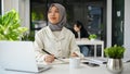 Charming Asian Muslim female office worker daydreaming, looking out the window