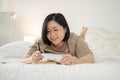 A charming Asian plus-size woman is keeping her diary while lying on her bed in her bedroom Royalty Free Stock Photo