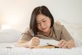 A charming Asian plus-size woman is keeping her diary while lying on her bed Royalty Free Stock Photo