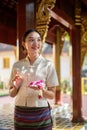 A charming Asian Thai woman in a traditional Thai-Lanna dress is in a temple, making a merit