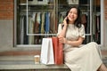 A charming Asian woman is on the phone while sitting on the stairs in front of the clothing store Royalty Free Stock Photo