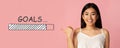 Charming Asian woman pointing at GOALS loading progress bar on pink studio background, panorama. Collage Royalty Free Stock Photo