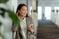Charming Asian woman with a smile standing holding mobile phone at the office and looking away Royalty Free Stock Photo