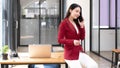 Charming Asian woman with a smile standing holding papers and mobile phone at the office. Royalty Free Stock Photo