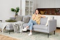 Charming asian woman talking on the smartphone sitting on the cozy couch at home. Smiling young woman chatting with