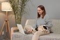 Charming attractive Caucasian woman wearing striped shirt sitting on sofa with her puppy dog using laptop computer browsing Royalty Free Stock Photo