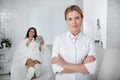 Charming beautician standing in her cabinet wile client resting on daybed