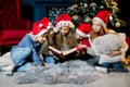 Charming and beautiful little children in Santa`s hats are reading Christmas stories and laughing, on the background of