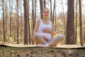 Charming beautiful pregnant woman doing yoga in nature outdoors sitting on yoga mat with crossed legs touching her belly looking Royalty Free Stock Photo