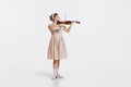 Charming beautiful young girl playing violin  over white studio background. Tender, lovely sound. Concept of Royalty Free Stock Photo