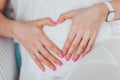 Charming tummy which the pregnant woman in a white dress embraces. The pregnant girl with pink manicure embracing belly Royalty Free Stock Photo