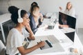 Charming black web-developer listening music in big headphones and using tablet. Indoor portrait of programmers working Royalty Free Stock Photo