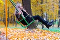 Charming blond girl on swing in autumn park