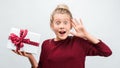 Charming blonde girl with gift posing with surprised face expression. Studio shot white background, isolated Royalty Free Stock Photo