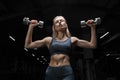 Charming blonde posing in the gym with dumbbells in her hands. View from below. The concept of sports, bodybuilding, fitness
