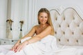 Charming Blonde Woman With Long Fair Hair In Underwear Sitting On Bed In Bright Rich Interior. Life After Forty Concept