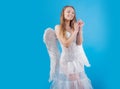 Charming blonde young woman in white dress and wings - angel cupid. Cute teen girl. Girl dressed as an angel on a light