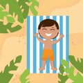 A charming boy in shorts lies on a blanket on the sand and sunbathes. The child is happy and cheerful and smiling. Royalty Free Stock Photo