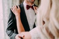 Charming bride fixes red bow tie on groom`s neck while they stand near the window. Wedding.