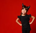 Little girl with devil horns, in black blouse and leggings. She laughing, hands on hips, posing on red background. Close up Royalty Free Stock Photo