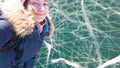 Charming brunette girl traveler takes a selfie standing on the clear bright ice of lake Baikal. Travel to Siberia.