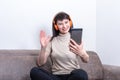 Charming brunette woman wearing orange headphones having a video call and showing a hello or bye gesture Royalty Free Stock Photo