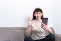 Charming brunette woman wearing orange headphones having a video call and showing a hello or bye gesture Royalty Free Stock Photo