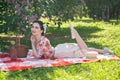A charming brunette young girl enjoys a rest and a picnic on the green summer grass alone. pretty woman have a holiday and spend v