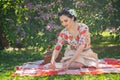 A charming brunette young girl enjoys a rest and a picnic on the green summer grass alone. pretty woman have a holiday and spend v Royalty Free Stock Photo