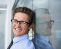 Charming businessman. A handsome young businessman leaning against a glass wall and smiling at you.