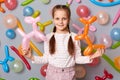 Charming calm little girl with pigtails standing against gray decorated wall holding multicolored balloons in hands, being in