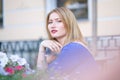 Charming caucasian blonde girl in a blue dress sitting at a table in a city cafe alone and waiting Royalty Free Stock Photo