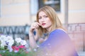 Charming caucasian blonde girl in a blue dress sitting at a table in a city cafe alone and waiting Royalty Free Stock Photo