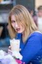 Charming caucasian blonde girl in a blue dress sitting at a table in a city cafe alone and waiting Royalty Free Stock Photo