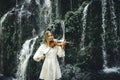 Charming Caucasian woman playing violin near waterfall. Music and art concept. Female wearing white dress in nature. Water splash Royalty Free Stock Photo