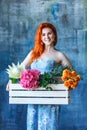 Charming cheerful red hair female shop assistant holds wooden box with flowers with Hydrangea purple, freesia, protea, roses