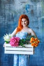 Charming cheerful red hair female shop assistant holds wooden box with flowers with Hydrangea purple, freesia, protea, roses