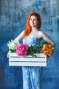 Charming cheerful red hair female shop assistant holds wooden box with flowers with Hydrangea purple, freesia, protea, roses