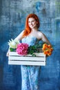 Charming cheerful red hair female shop assistant holds wooden box with flowers with Hydrangea purple, freesia, protea, roses