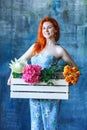 Charming cheerful red hair female shop assistant holds wooden box with flowers with Hydrangea purple, freesia, protea, roses