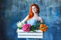 Charming cheerful red hair female shop assistant holds wooden box with flowers with Hydrangea purple, freesia, protea, roses