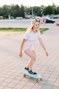 Charming and cheerfull girl longboarding in the park, she is wearing light pink shorts