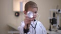 Charming child with toothy smile standing in hospital stretching stethoscope posing. Portrait of positive Caucasian