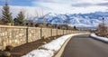 Charming Commute - A Road Flanked by a Stone Brick Wall, Revealing a Neighborhood with Mountain Views and a Cloudy Sky