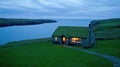 A charming cottage with a grass-covered roof glows warmly at night, nestled on a cliff by the ocean, inviting Royalty Free Stock Photo