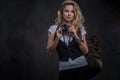 Charming curly blonde female dressed in a white t-shirt and waistcoat wears a lot of accessories and wristwatch, posing