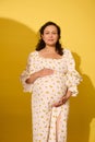 Charming pregnant woman in white summer sundress, stroking her belly in the ninth month of happy carefree pregnancy