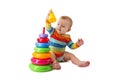 Charming cute baby in overalls plays with a colored plastic pyramid sitting on a white background. A child collects a colored