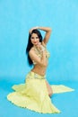 Charming dancer performs oriental belly dance on a blue background. A girl in a yellow beautiful dress is dancing an oriental bell Royalty Free Stock Photo