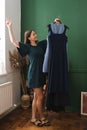 Young woman holding dresses on hanger, trying to decide what to wear.